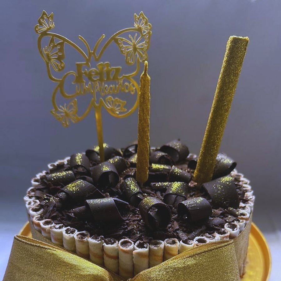 Torta de cumpleaños de chocolate con cigarrillos, moño dorado y cartel de Feliz Cumpleaños