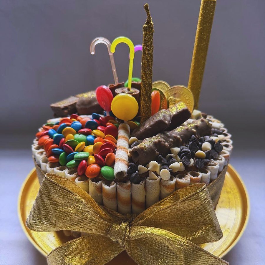 Torta de cumpleaños infantil con golosinas, M&M y moño dorado
