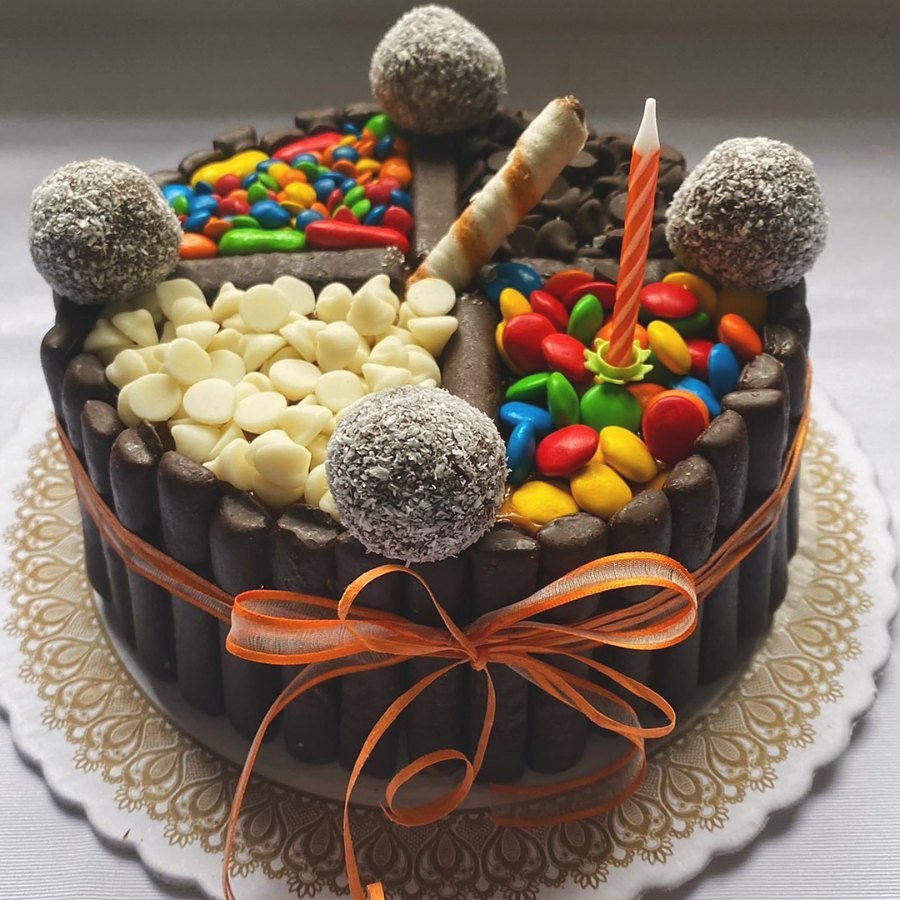 Torta de cumpleaños infantil cubierta de golosinas y bombones, con moño naranja