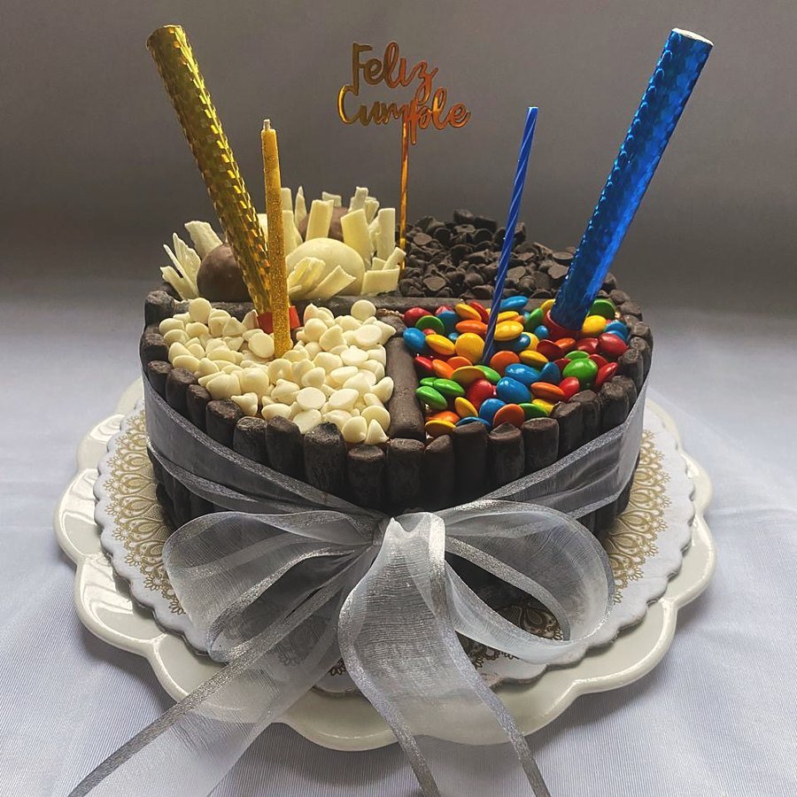 Torta de cumpleaños mitad rulos de chocolate blanco y mitad M&M, con moño plateado