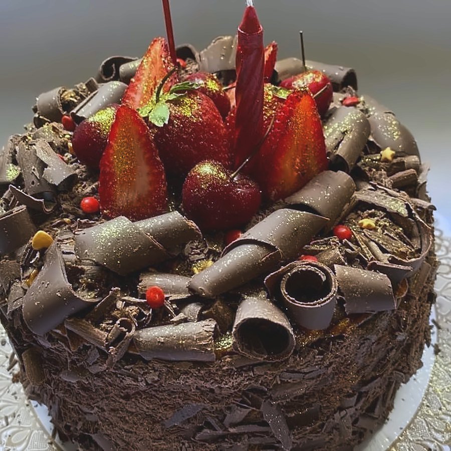 Torta de cumpleaños cubierta de rulos de chocolate, con frutillas y brillo dorado